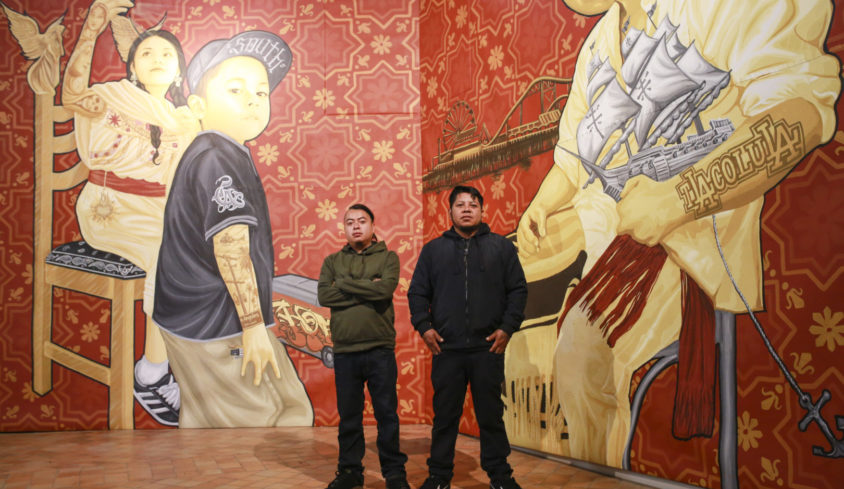 Cosijosea Cernas (à gauche) et Dario Canul (à droite) devant l’une de leurs peintures murales (originellement exposées à Los Angeles) ici au musée de l’hospice Comtesse de Lille.